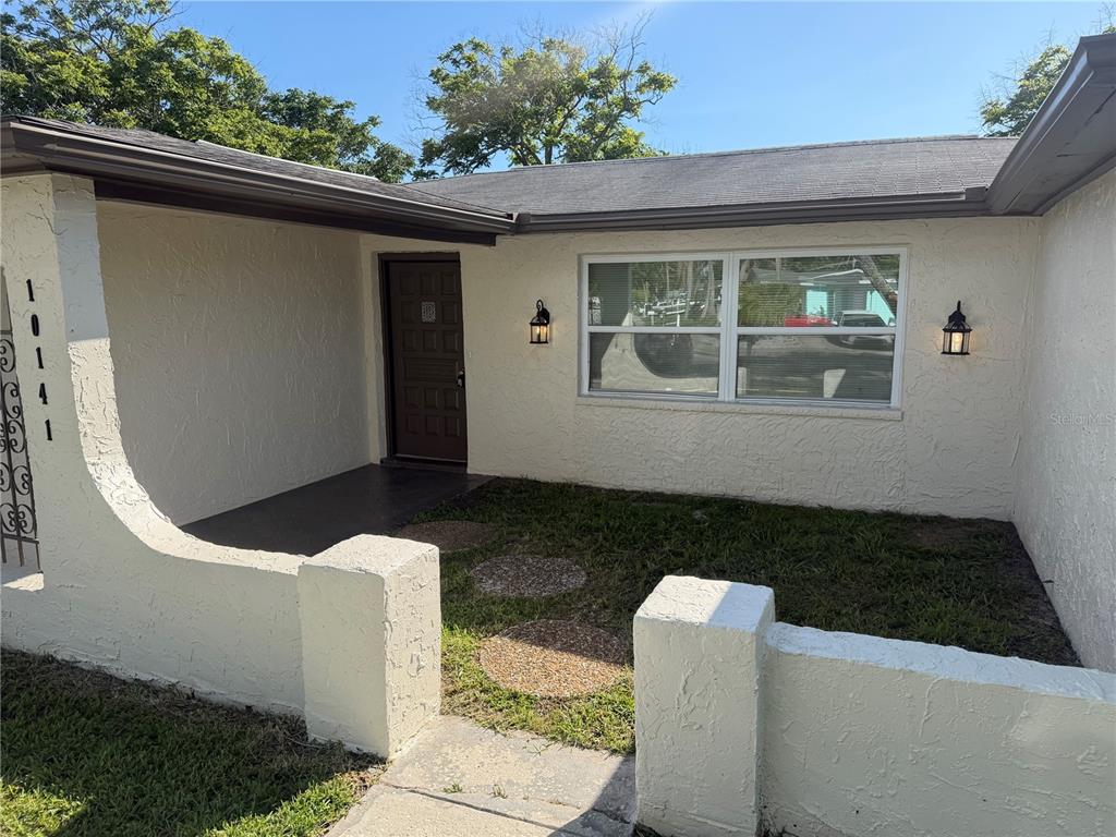The exterior of a house features a stucco facade, a small front courtyard, and a door — 10141 OLD HICKORY LANE, PORT RICHEY, FL