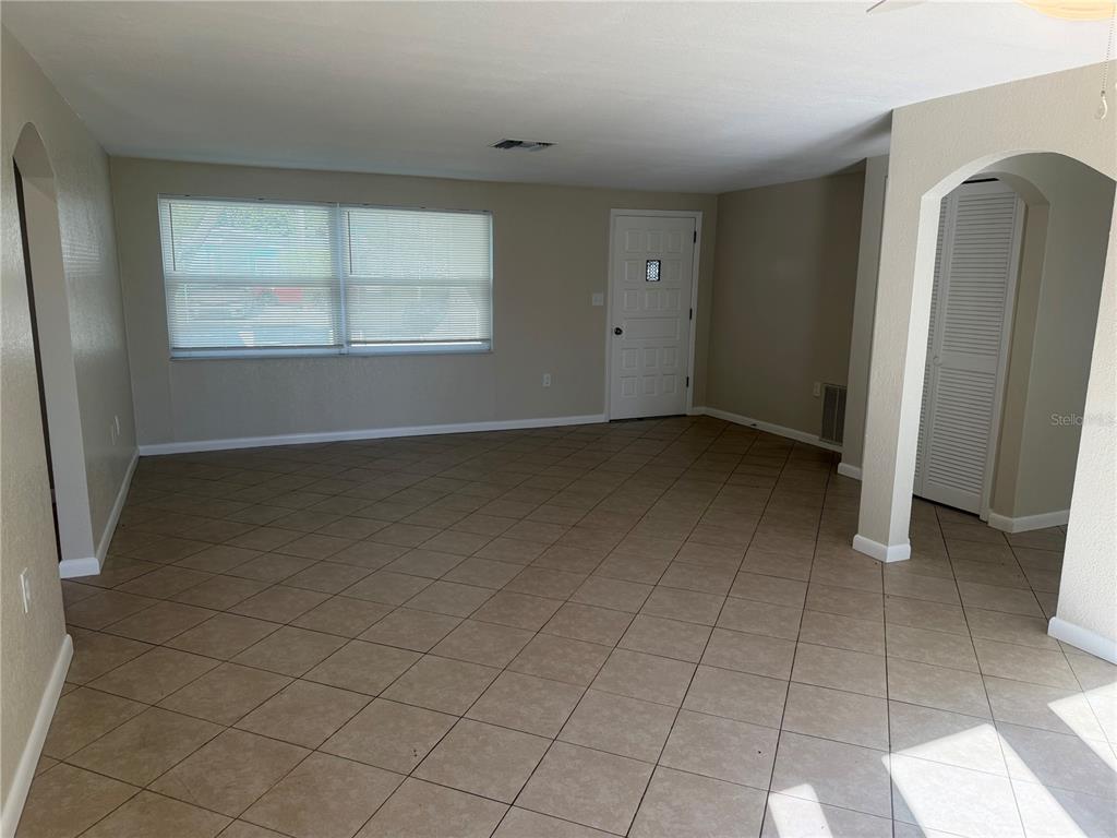 An empty living room features beige tile flooring, light-colored walls, a window, and a door — 10141 OLD HICKORY LANE, PORT RICHEY, FL