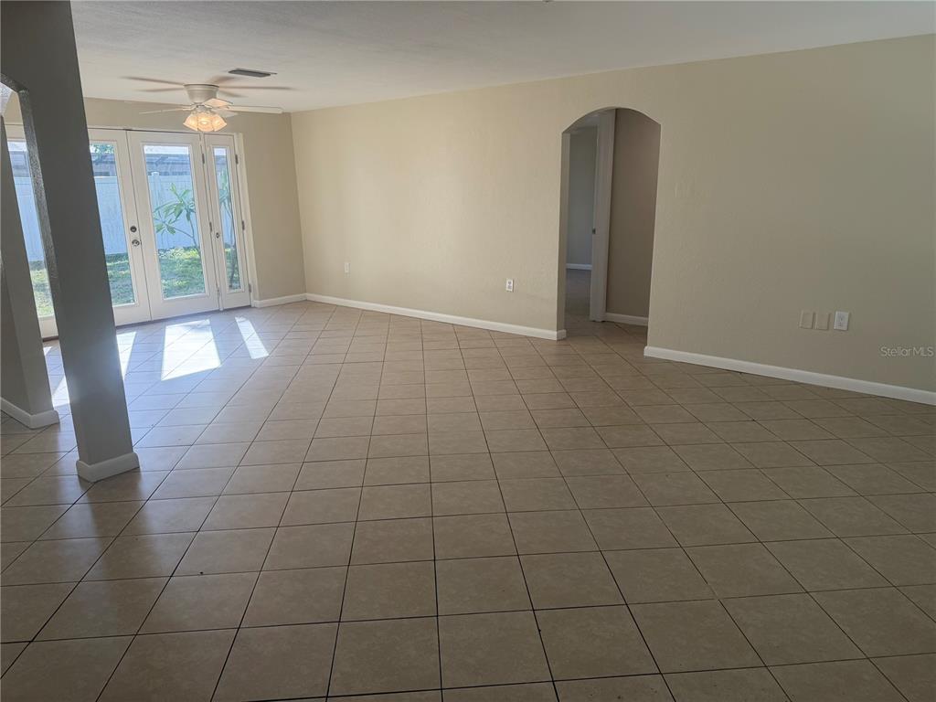 An empty room with beige tile flooring, a ceiling fan, and glass doors to outside — 10141 OLD HICKORY LANE, PORT RICHEY, FL