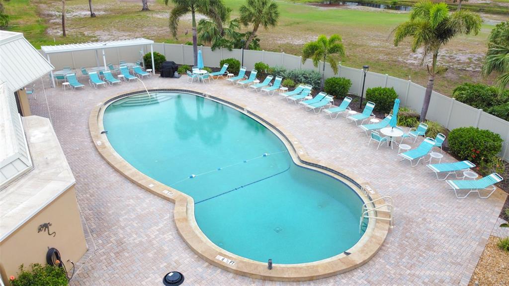 An aerial view shows a kidney-shaped swimming pool surrounded by a paved deck and lounge chairs — 4480 IRONWOOD CIRCLE UNIT 112A, BRADENTON, FL