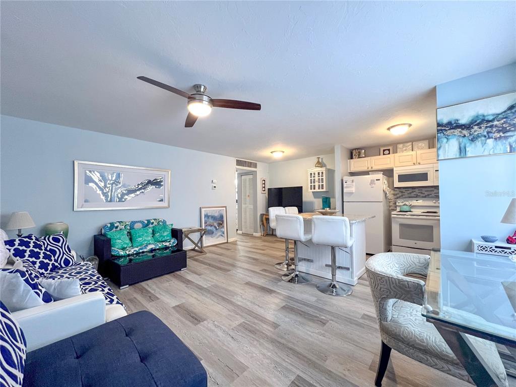 An open-concept living room and kitchen area featuring light wood-look flooring and white cabinetry — 4480 IRONWOOD CIRCLE UNIT 112A, BRADENTON, FL
