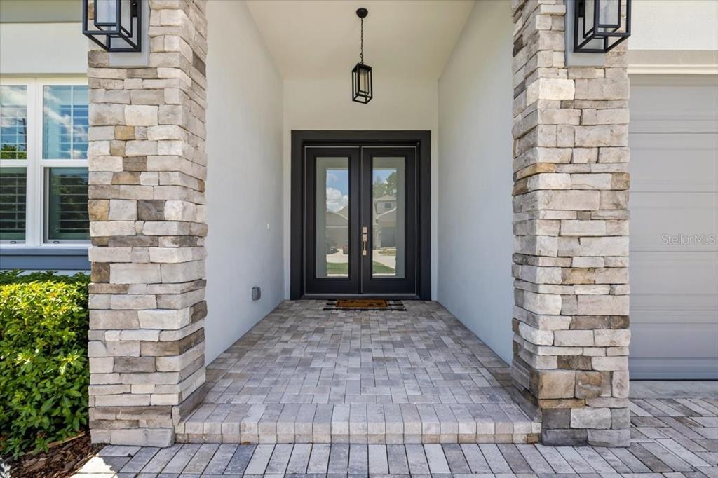 A stone-columned entryway features a double glass door, a hanging lantern, and paver flooring — 201 LAROCCA COURT, PALM HARBOR, FL