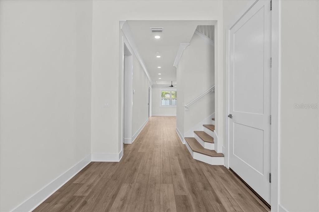 A bright hallway features light wood flooring, white walls, and a staircase with wooden treads — 201 LAROCCA COURT, PALM HARBOR, FL