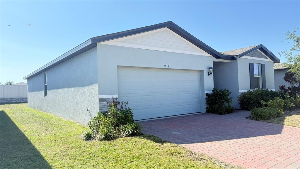 A single-story house with a gray stucco exterior, a brick paver driveway, and a garage — 2618 IRISH ELK AVENUE, DAVENPORT, FL