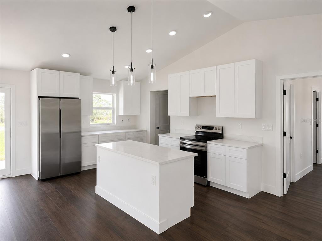 A modern kitchen features white cabinetry, stainless steel appliances, a center island, and dark flooring — 14973 NW 304TH STREET, OKEECHOBEE, FL