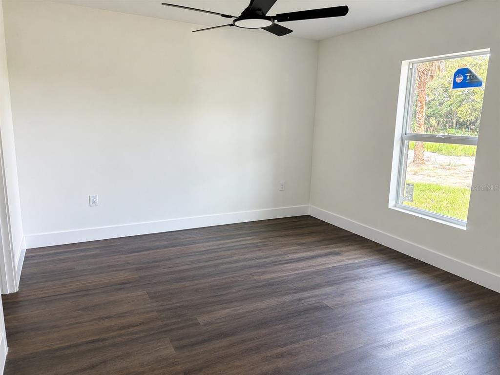 An empty bedroom features white walls, dark wood-look flooring, a ceiling fan, and a window — 14973 NW 304TH STREET, OKEECHOBEE, FL