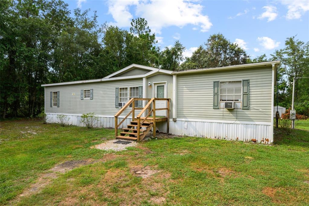 A light green single-wide mobile home with a wooden staircase leading to the front door — 9798 STATE ROAD 100 W, STARKE, FL