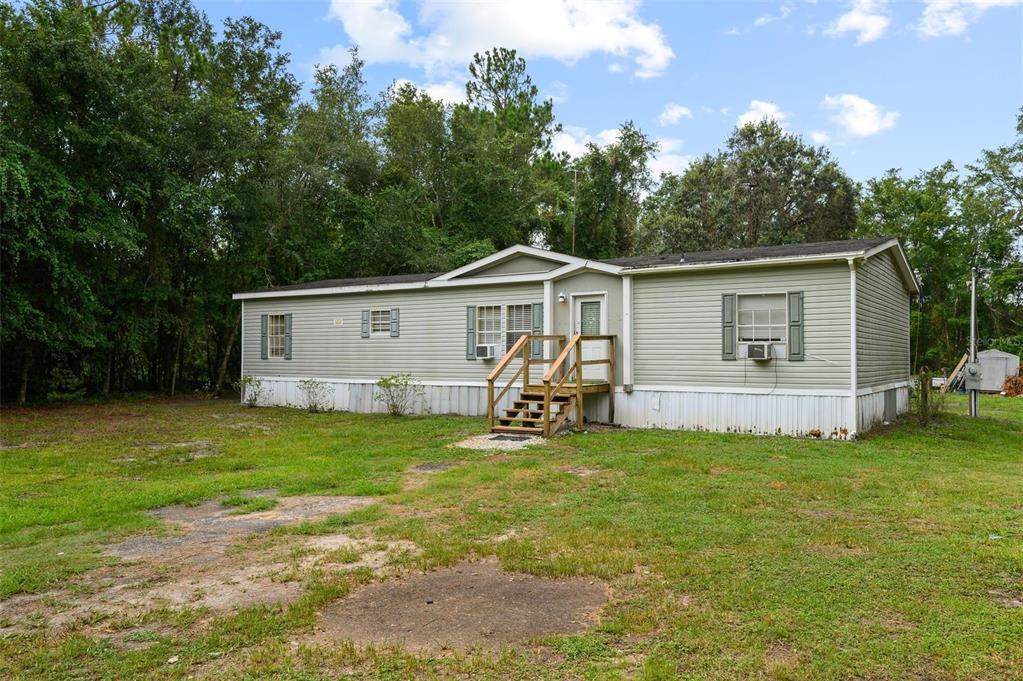 A single-story manufactured home with light green siding and a wooden front porch — 9798 STATE ROAD 100 W, STARKE, FL