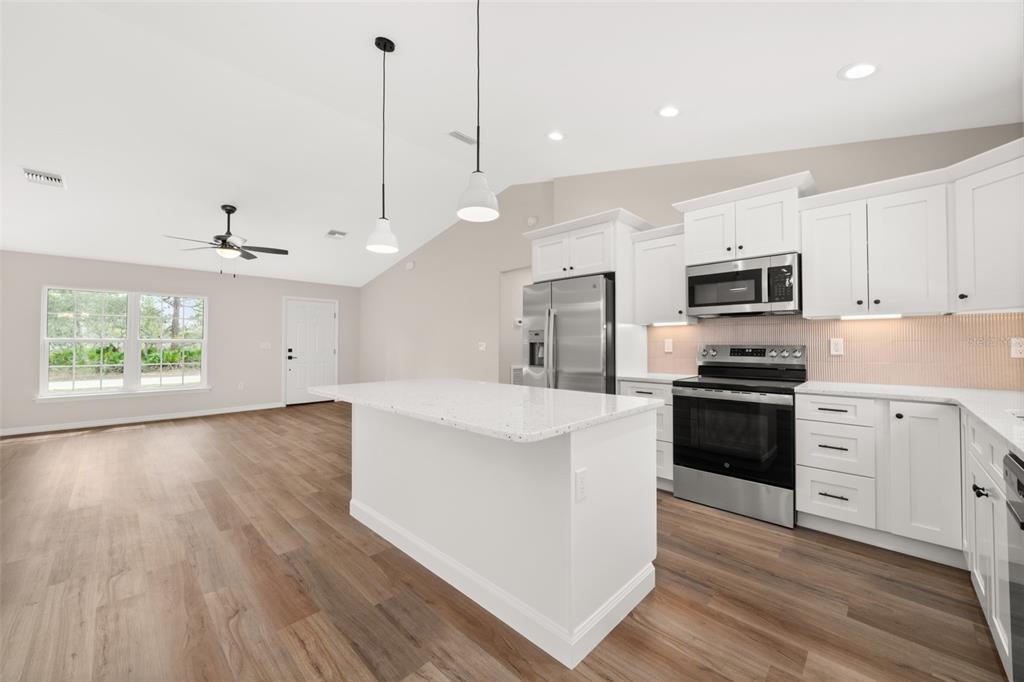 A kitchen with white cabinets, stainless steel appliances, and an island opens to a living area — 4206 JAGUAR DRIVE, SEBRING, FL