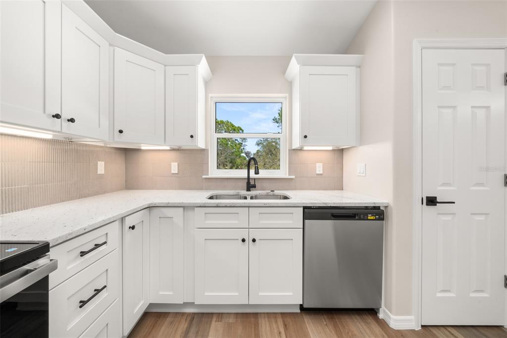 A kitchen features white cabinets, granite countertops, a stainless steel dishwasher, and a window — 4206 JAGUAR DRIVE, SEBRING, FL