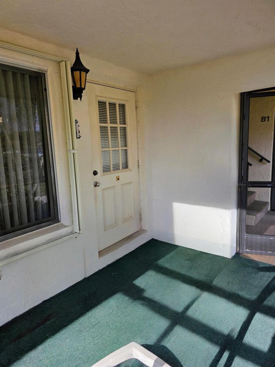 An exterior view of a building entrance featuring a white door, window, and green carpet — 423 Pine Glen Lane # 1, FL 33463, FL