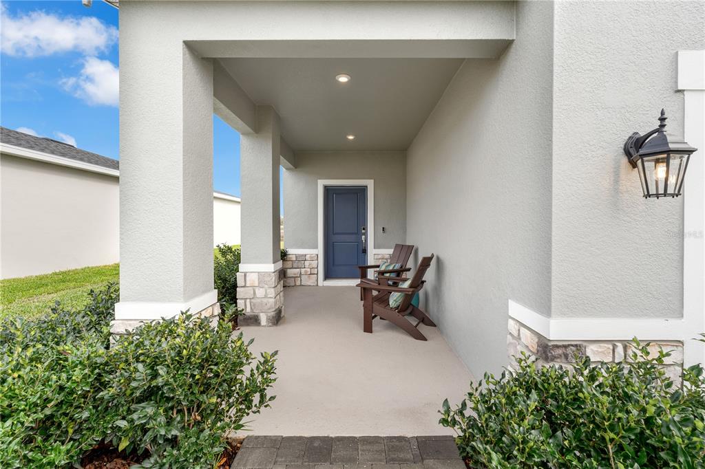 A covered front porch with stone accents, two chairs, and a blue front door — 10148 MORNING MEADOWLARK TRAIL, PARRISH, FL