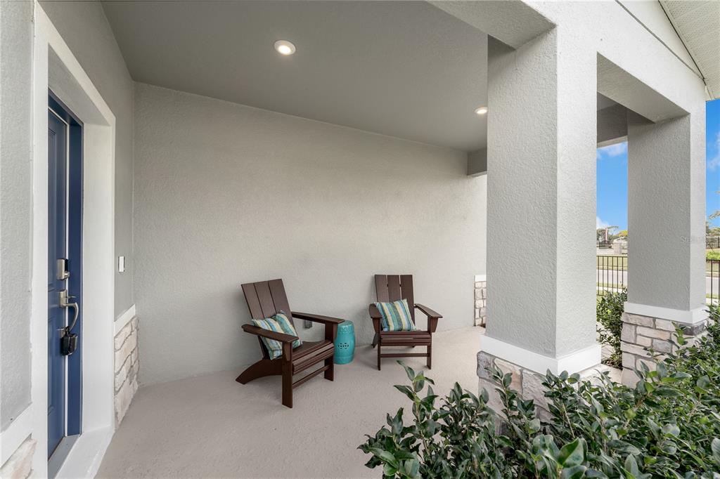 A covered front porch features two dark wooden chairs, a small teal table, and stone accents — 10148 MORNING MEADOWLARK TRAIL, PARRISH, FL