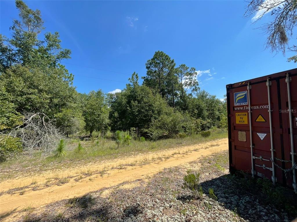 A dirt path leads toward a wooded area next to a large red shipping container — 5TH STREET UNIT 1, INTERLACHEN, FL