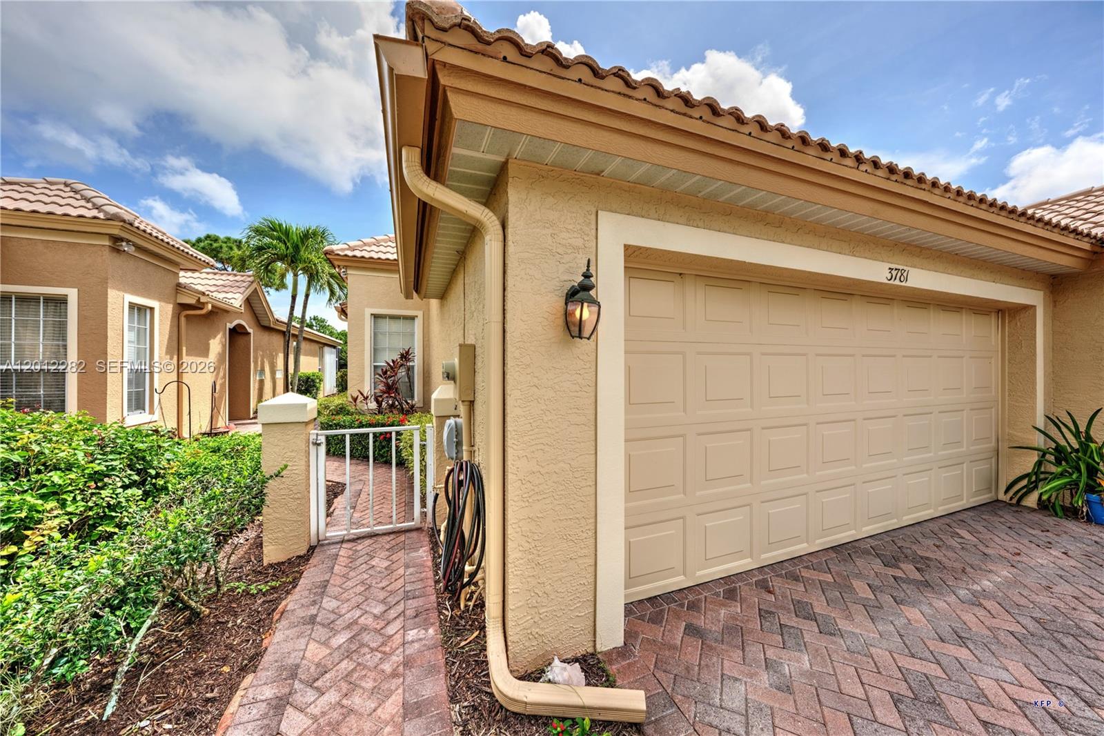 A beige stucco house exterior features a garage, a brick walkway, and a small gate — 3781 NW Willow Creek Dr, Jensen Beach FL 34957, JENSEN BEACH, FL