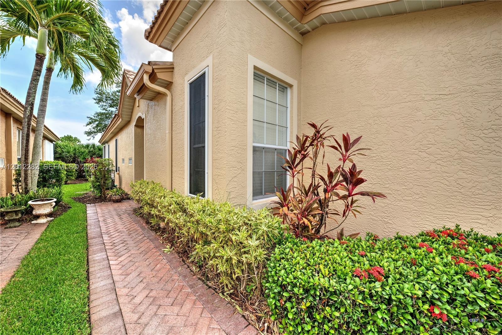 A brick walkway leads along the side of a beige stucco house with landscaping — 3781 NW Willow Creek Dr, Jensen Beach FL 34957, JENSEN BEACH, FL