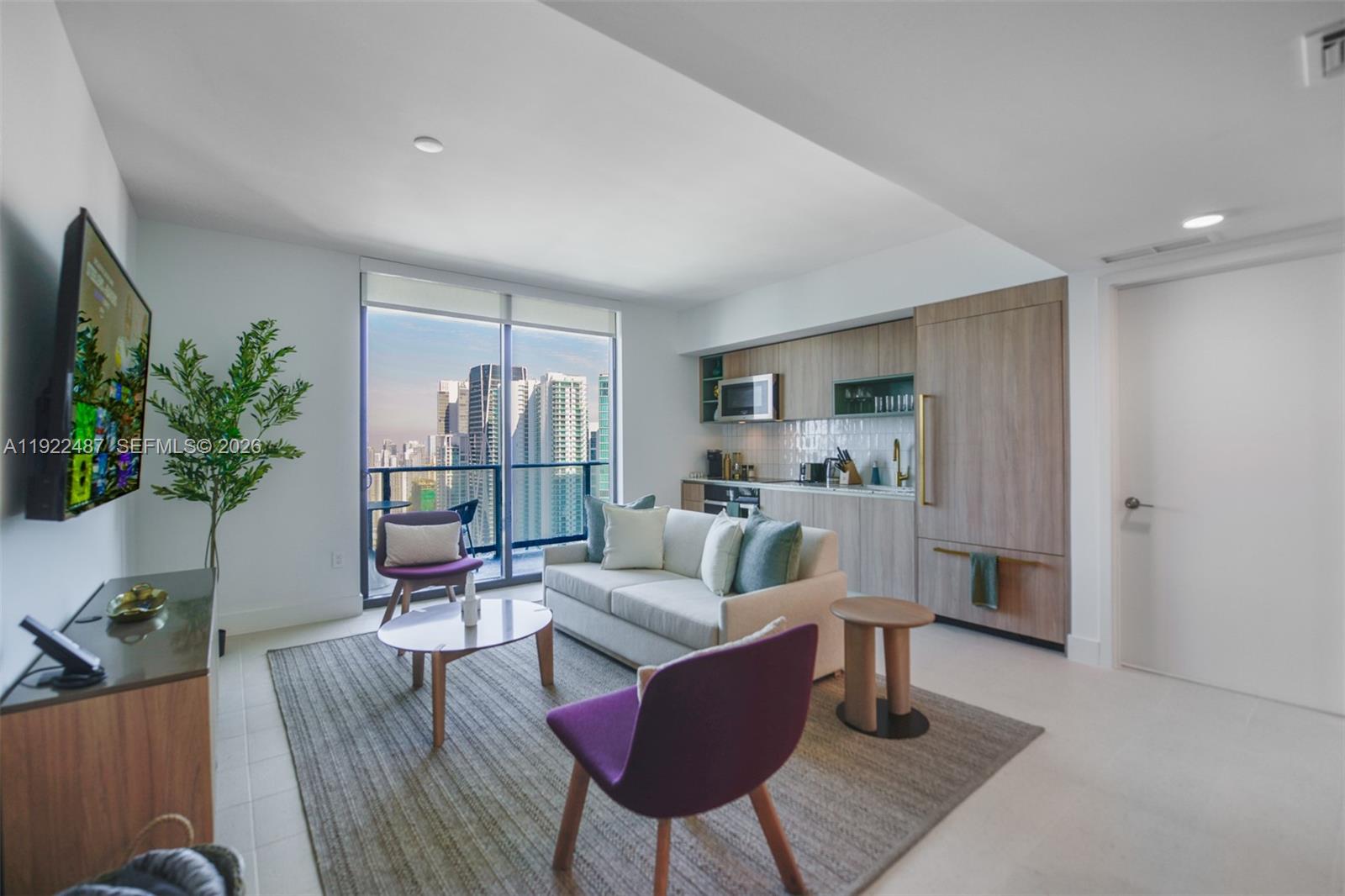 A modern living room features a kitchenette, a sofa, purple chairs, and a city balcony — 159 NE 6th St # 4601, Miami FL 33132, MIAMI, FL
