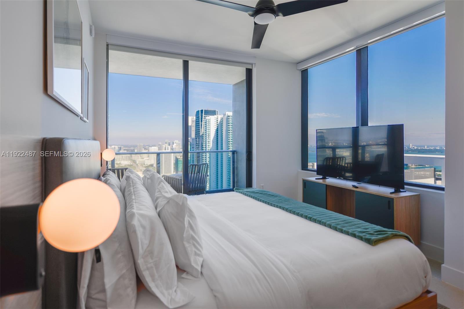 A modern bedroom features a bed, a television, and floor-to-ceiling windows overlooking a city skyline — 159 NE 6th St # 4601, Miami FL 33132, MIAMI, FL