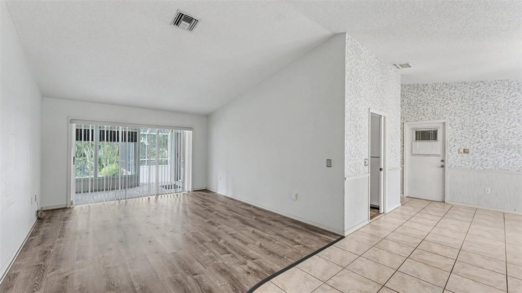 An open living area features wood-look flooring, tiled entryway, white walls, and sliding glass doors — 549 PENINSULAR DRIVE, LAKELAND, FL