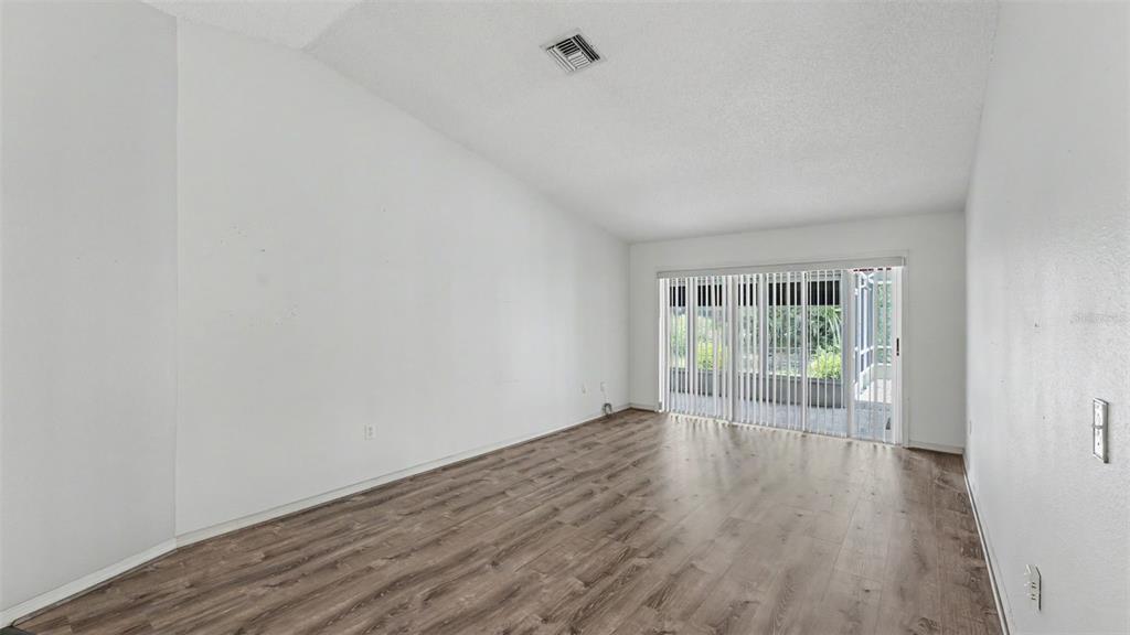 An empty room features white walls, wood-look flooring, and sliding glass doors leading outside — 549 PENINSULAR DRIVE, LAKELAND, FL