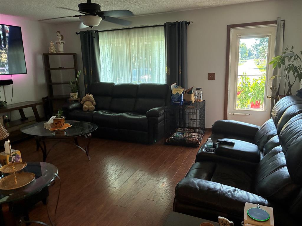 A living room features dark leather sofas, wood-look flooring, a ceiling fan, and a glass door — 10310 SW 91ST COURT, OCALA, FL