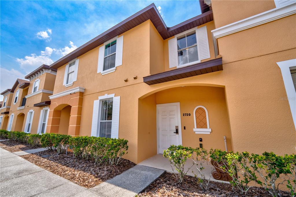 The exterior of a two-story tan stucco townhouse features white trim and a front entrance — 2720 ROADSTER, KISSIMMEE, FL