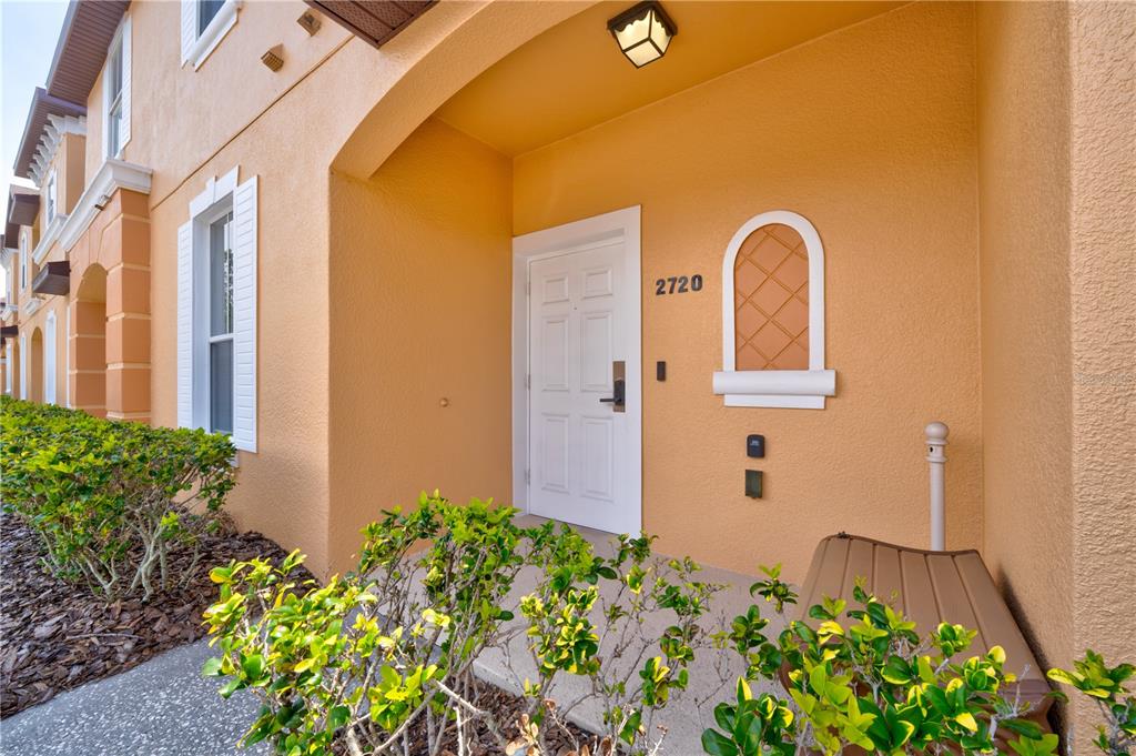 The exterior entrance of a tan stucco building features a white door and arched window — 2720 ROADSTER, KISSIMMEE, FL