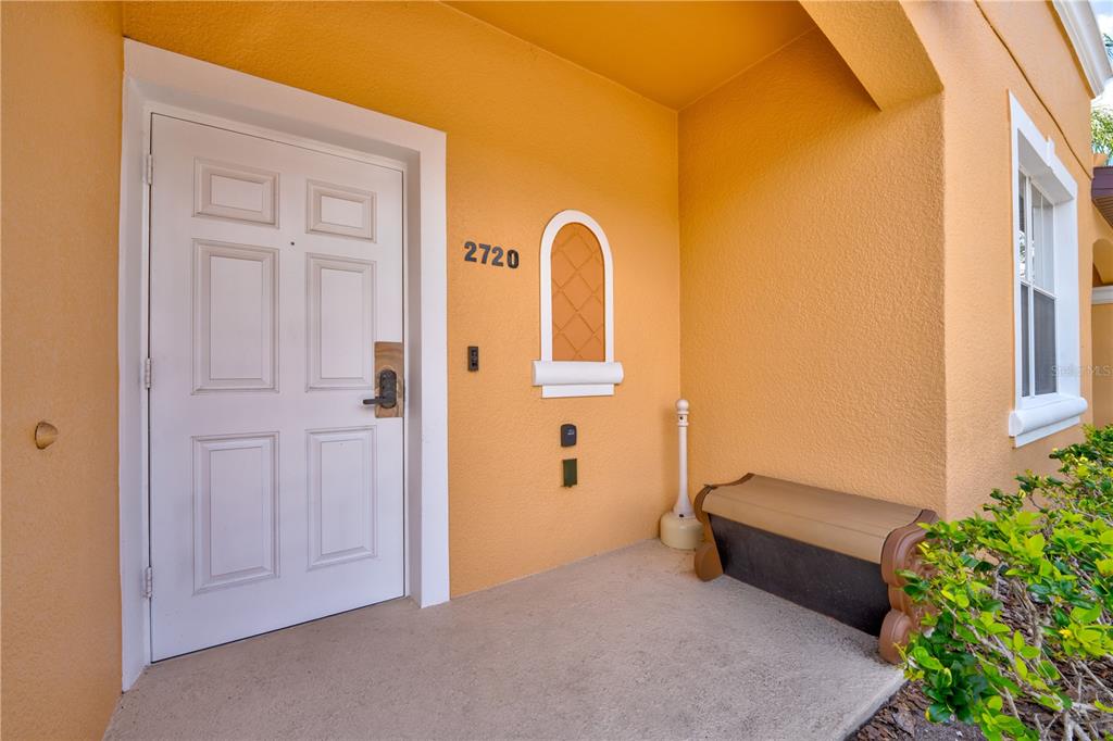 A white front door with a smart lock sits on a covered orange porch — 2720 ROADSTER, KISSIMMEE, FL