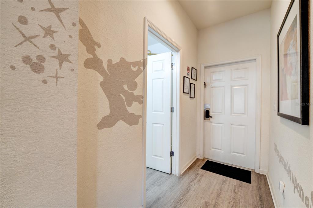 An entryway features light wood-look flooring, a white door, and a wall decal of Tinkerbell — 2720 ROADSTER, KISSIMMEE, FL
