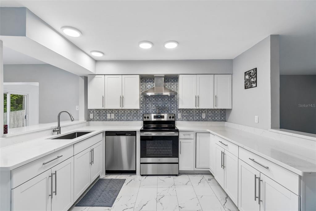A modern kitchen features white cabinetry, stainless steel appliances, quartz countertops, and patterned tile backsplash — 8120 BROWN PELICAN AVENUE, NEW PORT RICHEY, FL