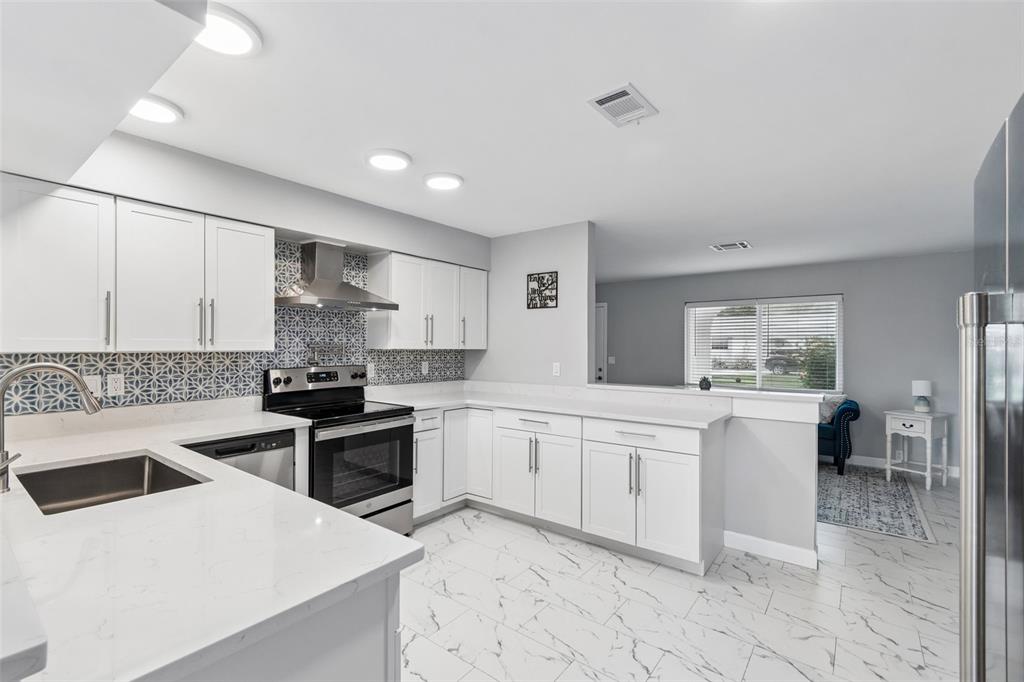 A modern kitchen featuring white cabinets, quartz countertops, a patterned backsplash, and light tile flooring — 8120 BROWN PELICAN AVENUE, NEW PORT RICHEY, FL