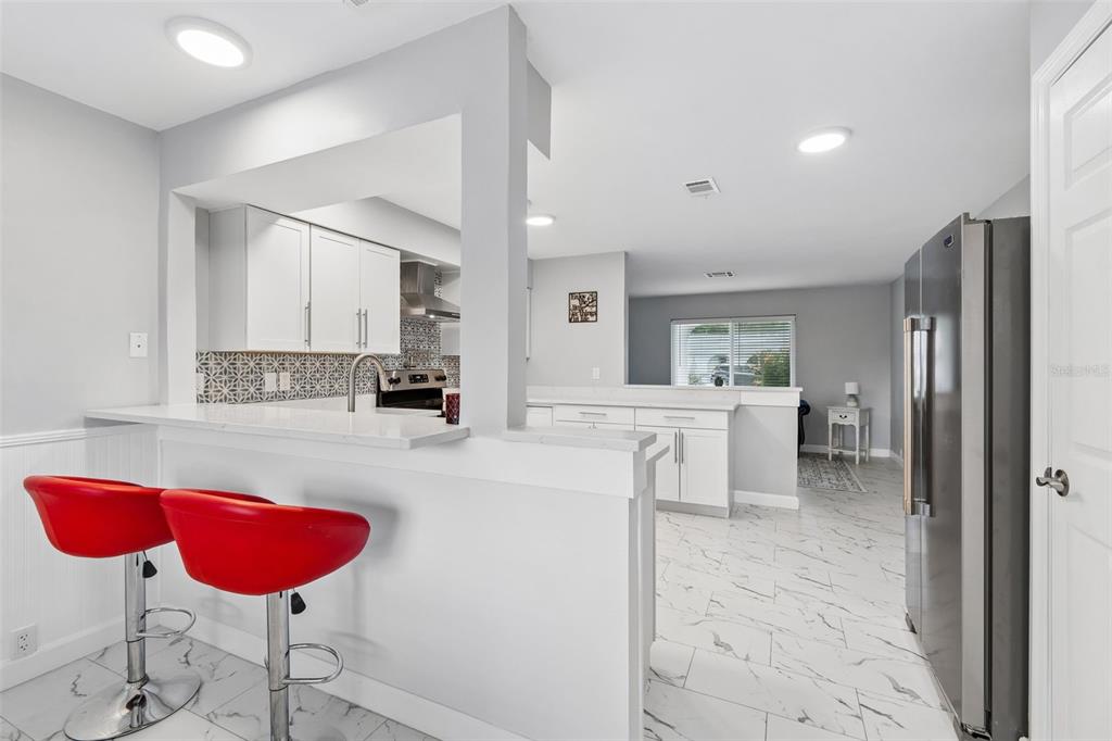 A kitchen with white cabinets, a breakfast bar with red stools, and marble-look tile flooring — 8120 BROWN PELICAN AVENUE, NEW PORT RICHEY, FL