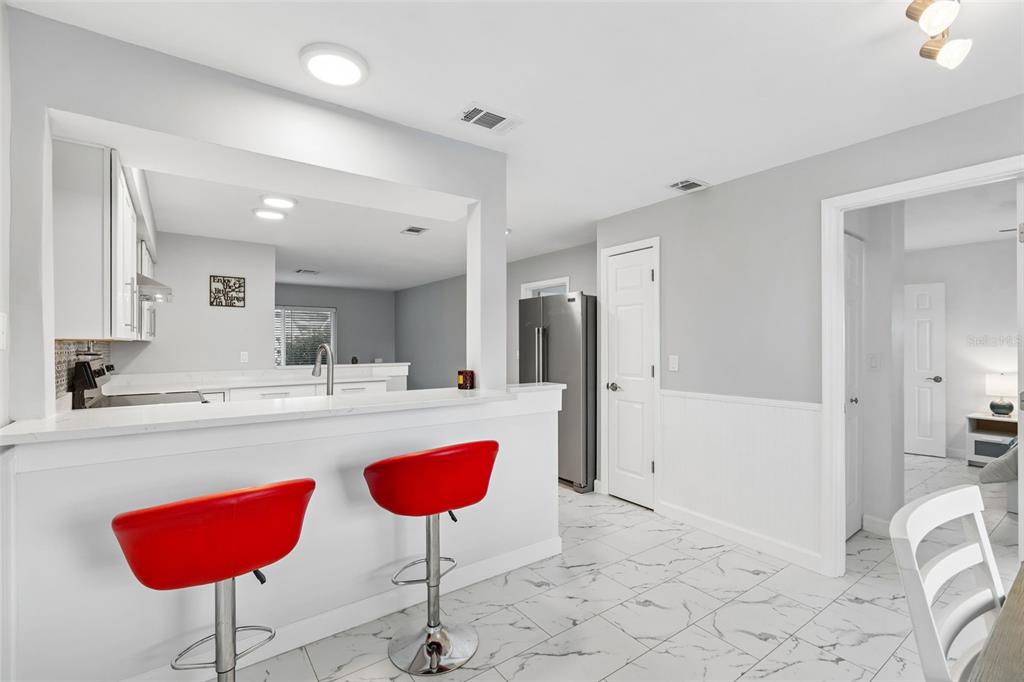 A kitchen with white cabinets, a breakfast bar with two red stools, and tiled floors — 8120 BROWN PELICAN AVENUE, NEW PORT RICHEY, FL