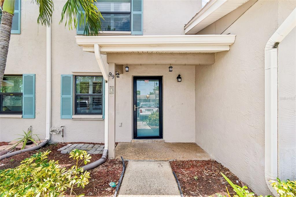 A beige exterior entrance features a glass storm door, blue shutters, and a concrete walkway — 2131 RIDGE ROAD S UNIT 99, LARGO, FL