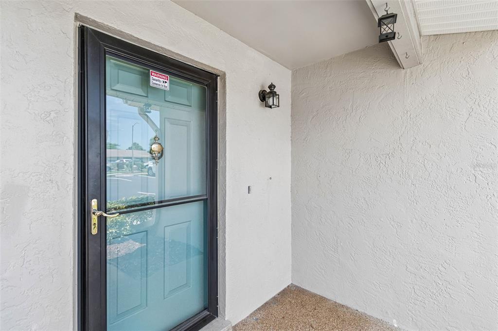 A front entryway features a black storm door with a security sticker and a light fixture — 2131 RIDGE ROAD S UNIT 99, LARGO, FL