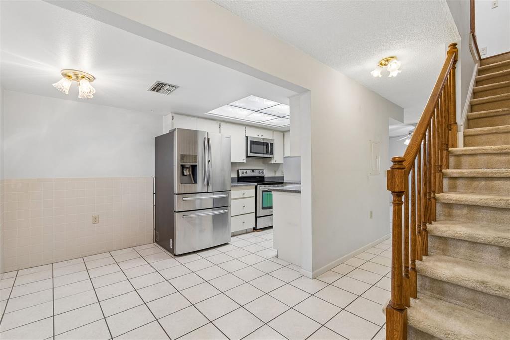 A kitchen with white cabinets, stainless steel appliances, and tile flooring next to carpeted stairs — 2131 RIDGE ROAD S UNIT 99, LARGO, FL