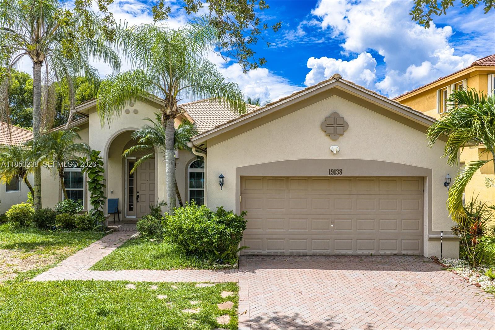 A single-story house features a beige stucco exterior, a tiled roof, and a two-car garage — 19138 Stonebrook St, Weston FL 33332, WESTON, FL