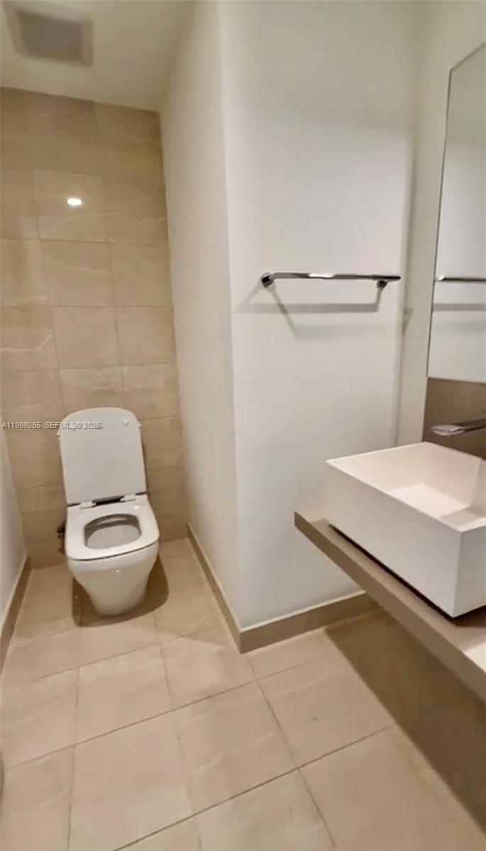 A modern bathroom features a white toilet, a vessel sink, and beige tile flooring — 1000 brickell plz # 2008, Miami FL 33131, MIAMI, FL