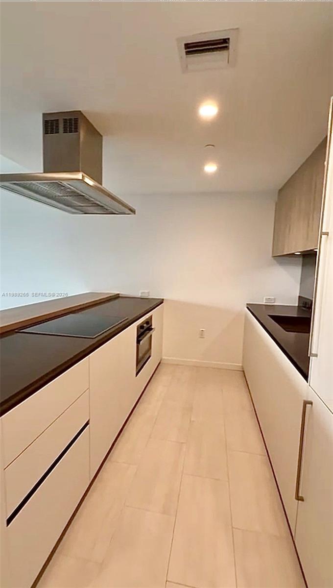 A modern galley kitchen features white cabinets, dark countertops, and a stainless steel range hood — 1000 brickell plz # 2008, Miami FL 33131, MIAMI, FL