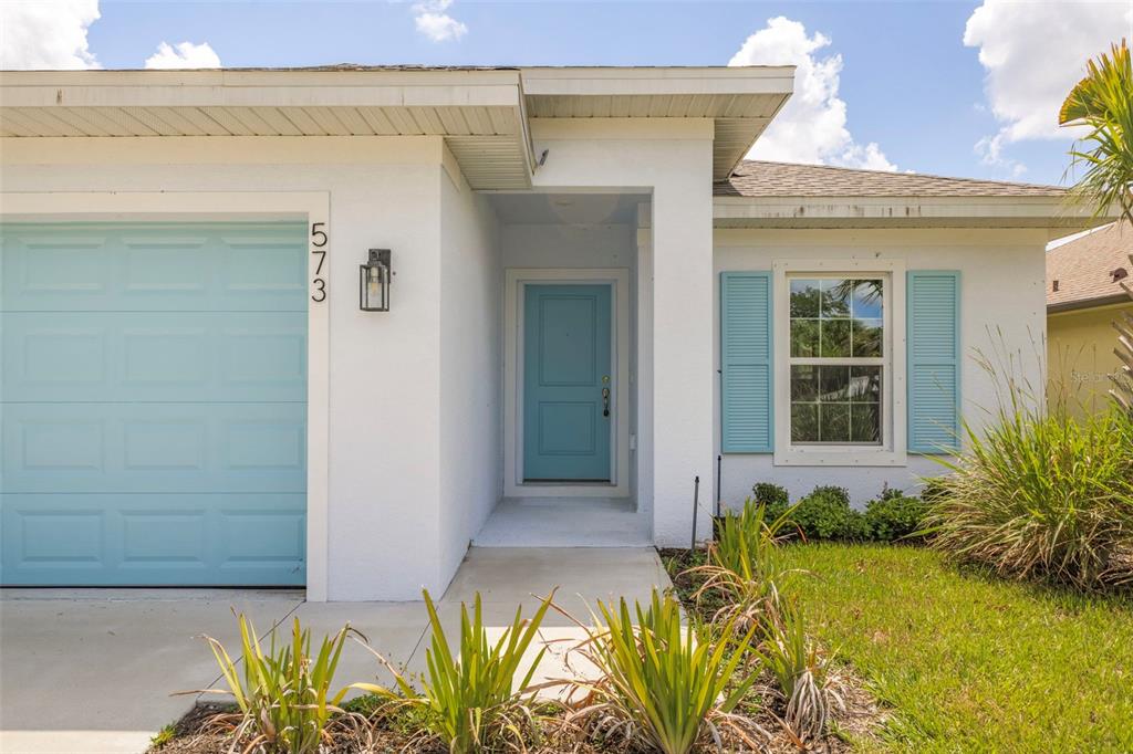 A single-story house exterior features a light blue garage door, front door, and window shutters — 573 ROSE APPLE CIRCLE, PORT CHARLOTTE, FL