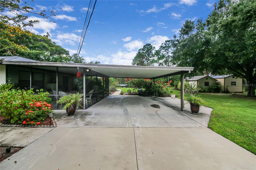 A concrete driveway leads to a covered carport attached to a house with a screened porch — 6168 ARBOREA DRIVE, INDIAN LAKE ESTATES, FL