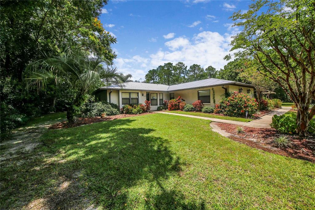 A single-story house with a metal roof, light-colored siding, and a landscaped front yard — 6168 ARBOREA DRIVE, INDIAN LAKE ESTATES, FL