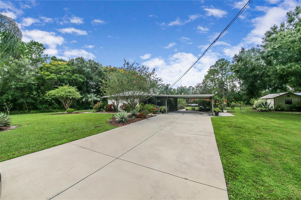 A concrete driveway leads to a single-story house with a carport and a large lawn — 6168 ARBOREA DRIVE, INDIAN LAKE ESTATES, FL