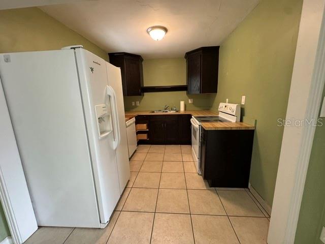A kitchen features dark wood cabinets, a white refrigerator, and light-colored tile flooring — 2976 POPLAR STREET, SARASOTA, FL