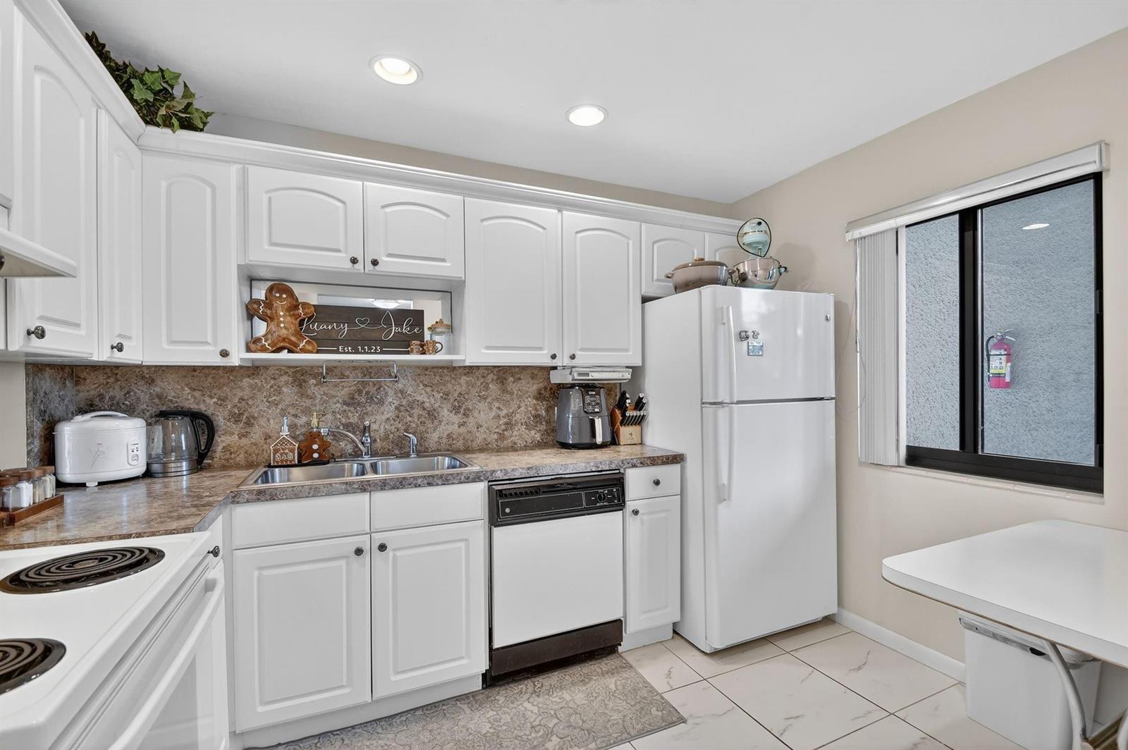 A kitchen features white cabinets, a brown stone-look backsplash, and a white refrigerator — 4272 Deste Court # 106, Lake Worth FL 33467, LAKE WORTH, FL