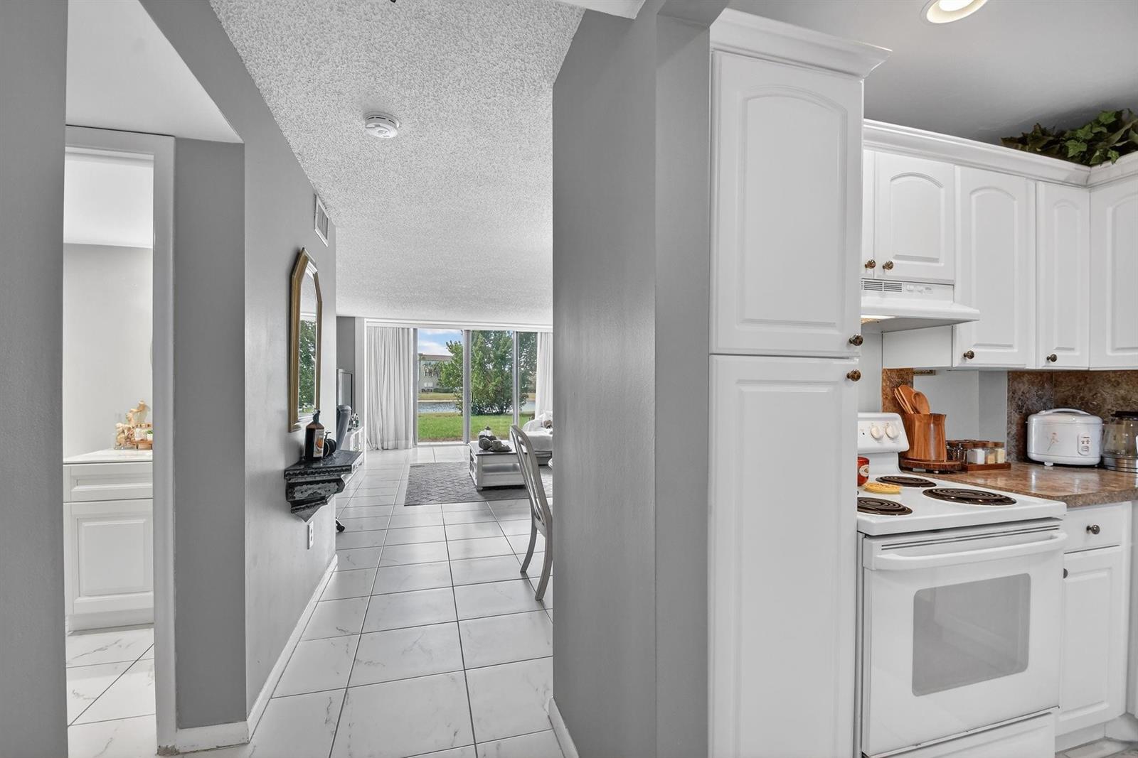 A view from a white kitchen looking through a hallway toward a living room — 4272 Deste Court # 106, Lake Worth FL 33467, LAKE WORTH, FL