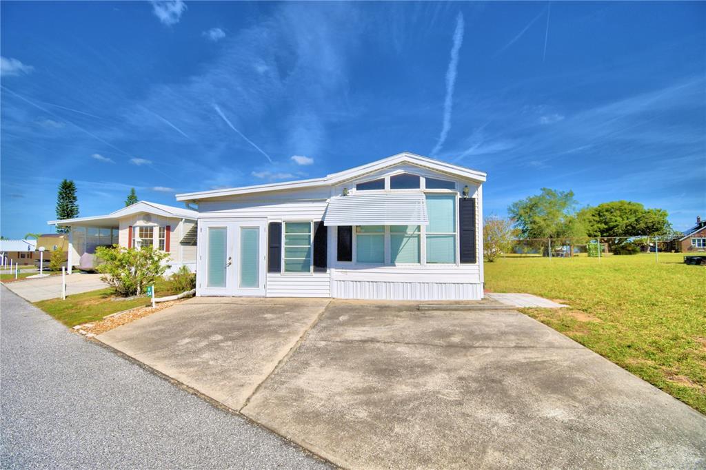 A white manufactured home with a concrete driveway sits under a bright blue sky — 251 PATTERSON ROAD UNIT H54, HAINES CITY, FL