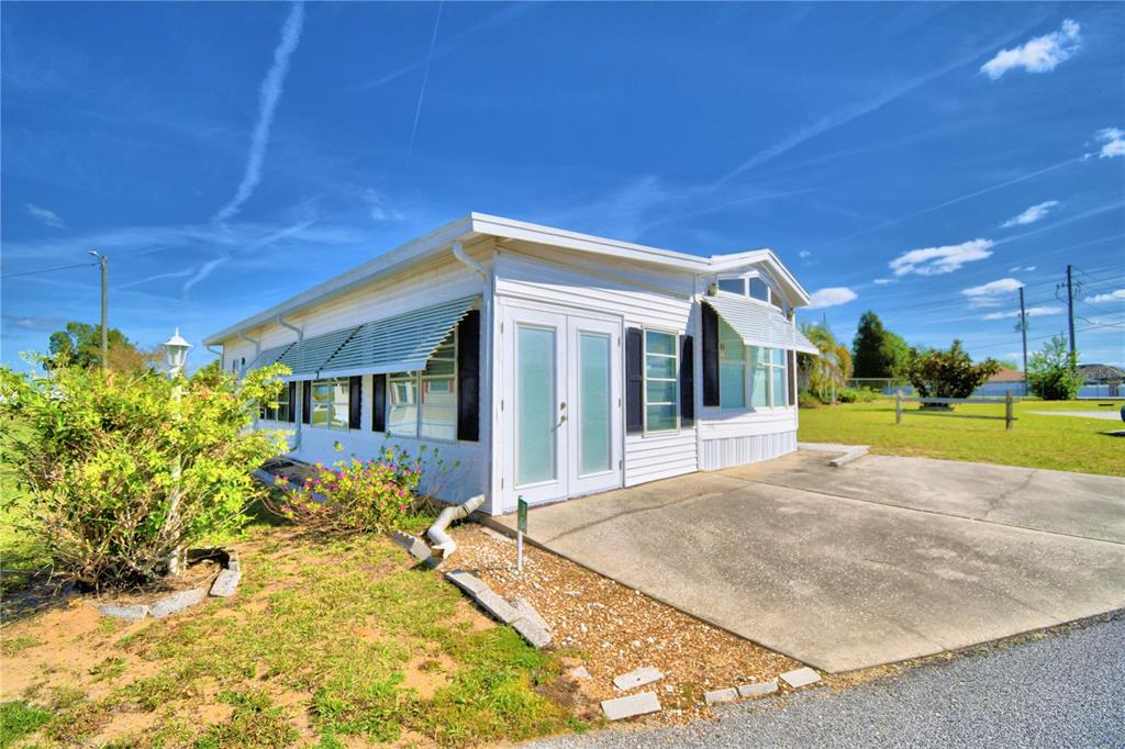 A white mobile home with a concrete driveway and metal window awnings under a blue sky — 251 PATTERSON ROAD UNIT H54, HAINES CITY, FL