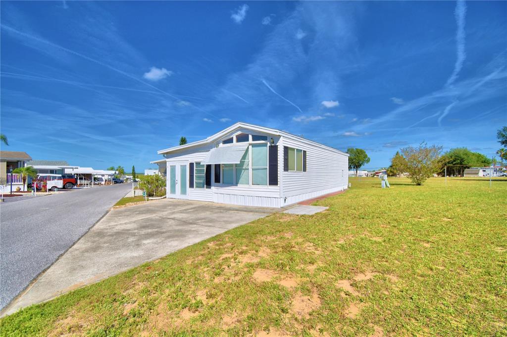 A white manufactured home with a concrete driveway sits on a grassy lot under blue skies — 251 PATTERSON ROAD UNIT H54, HAINES CITY, FL