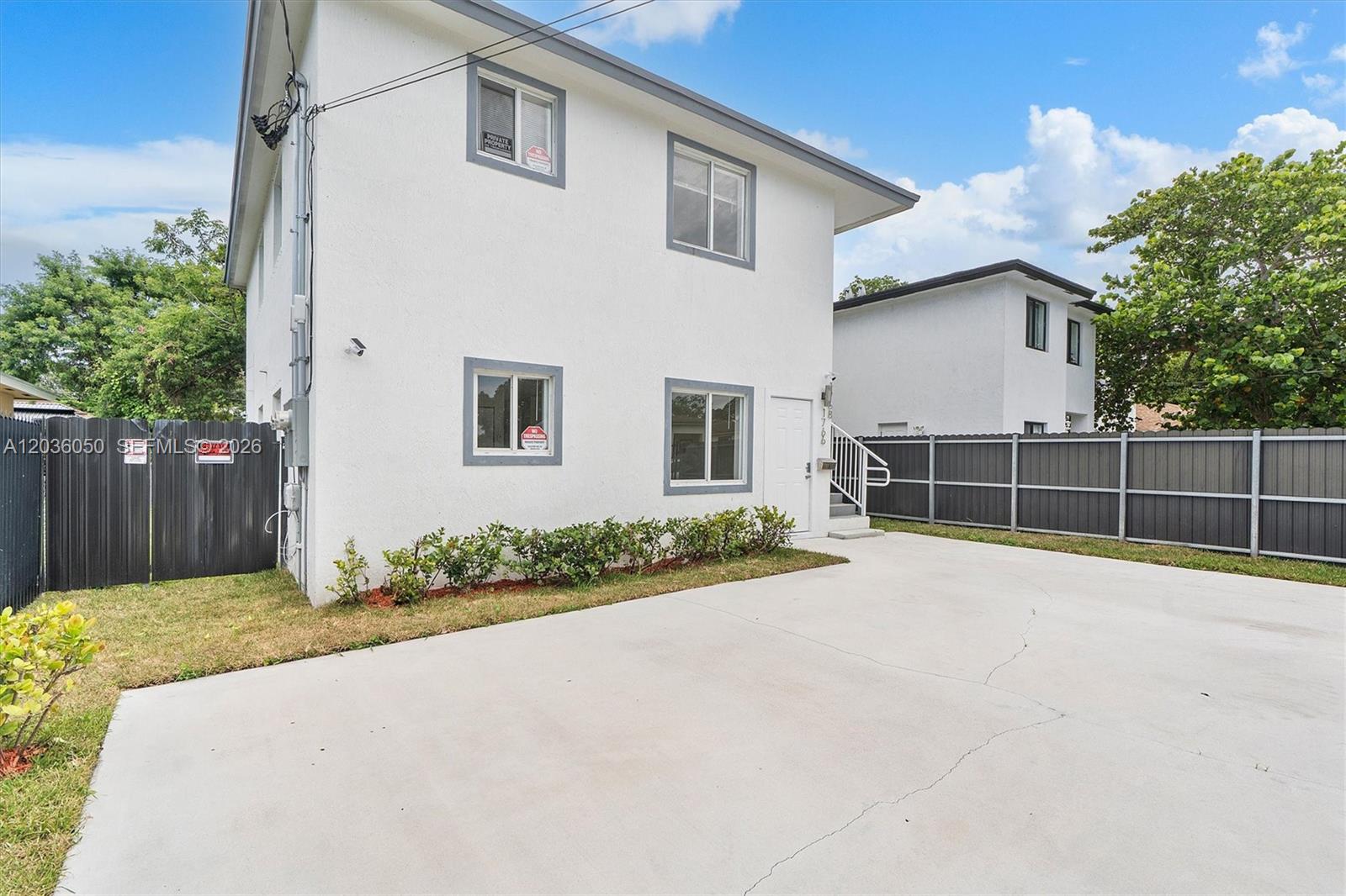 A two-story white building with gray trim stands behind a concrete driveway and fence — 1766 NW 68th Ter, Miami FL 33147, MIAMI, FL